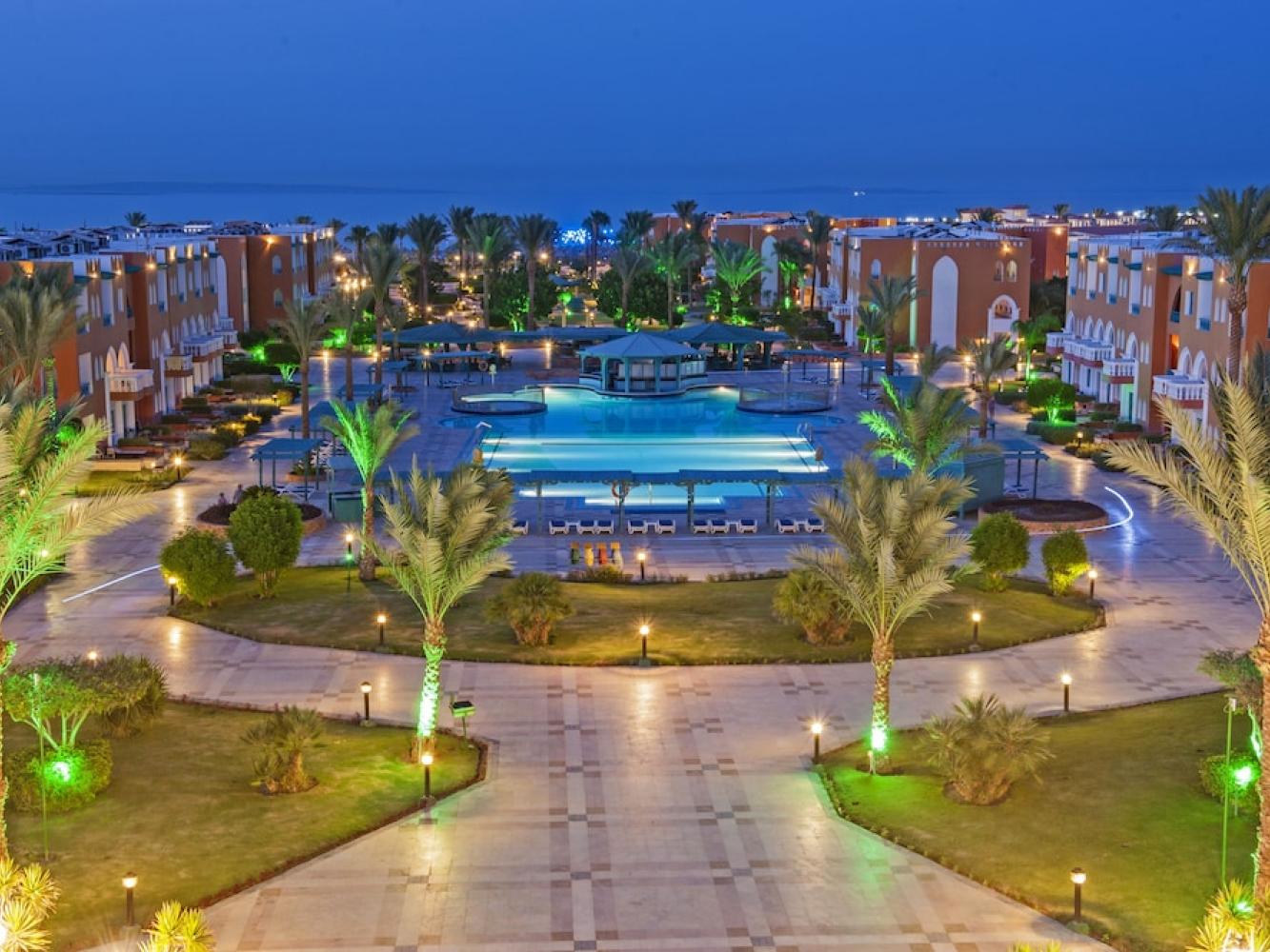 SUNRISE Garden Beach Resort in Hurghada in der Abenddämmerung, beleuchtete Poolanlage zwischen Palmen, dahinter das Rote Meer