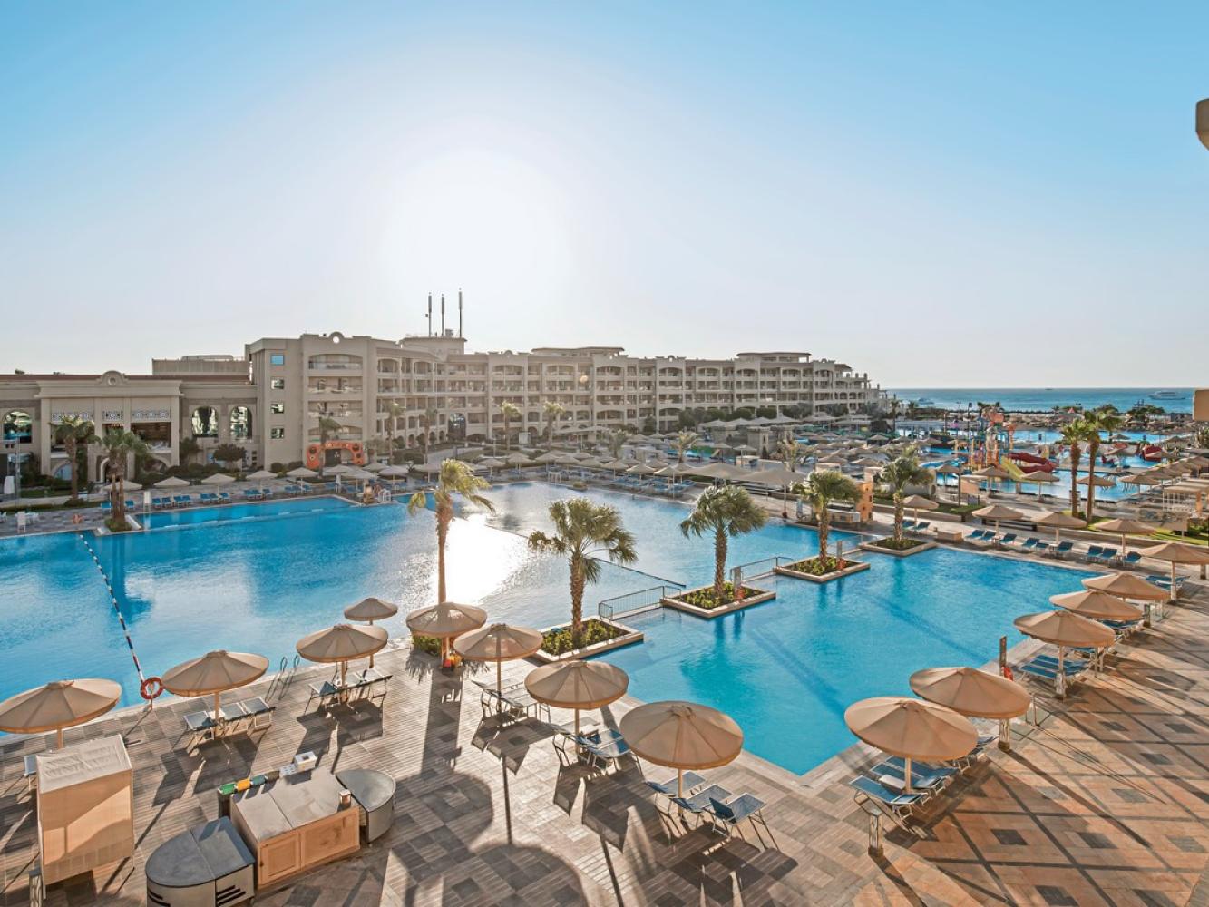 Pickalbatros White Beach Resort in Hurghada, große Poollandschaft mit Sonnenschirmen vor dem Hotelgebäude, rechts das Rote Meer